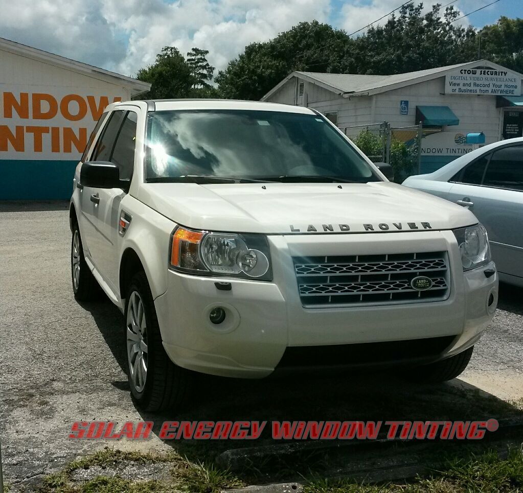 A white Land Rover SUV parked in a lot in front of a building with a Solar Energy Window Tinting sign.
