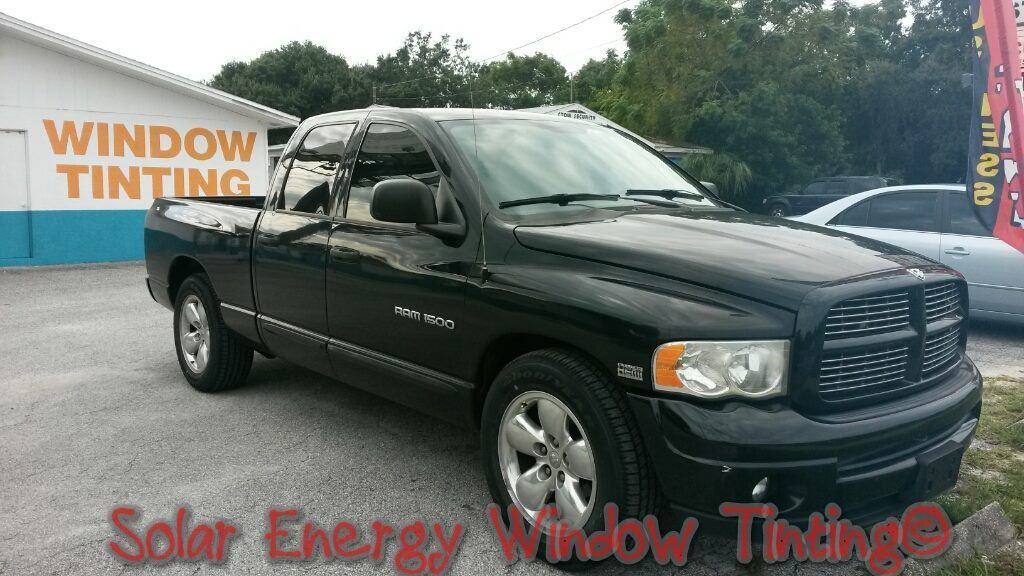 A black Dodge Ram pickup truck parked in front of a building with a WINDOW TINTING sign.