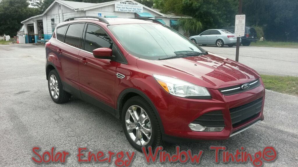 A red Ford Escape SUV parked on a gravel lot with freshly tinted windows, viewed from the front passenger side.