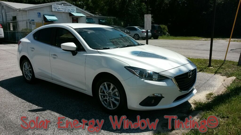 A white Mazda parked outside a business with the text Solar Energy Window Tinting overlaid on the bottom of the image.