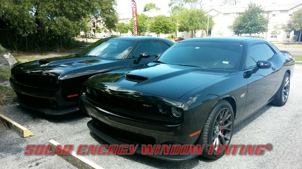 Two black Dodge Challenger cars parked outdoors in a lot, showcasing tinted windows.