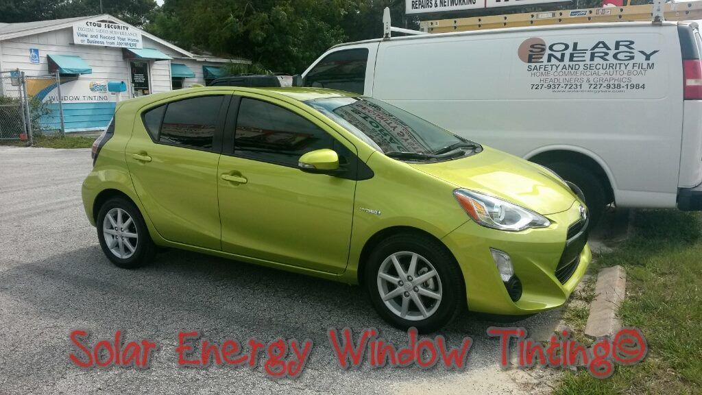 A bright green hatchback parked on a gravel lot next to a white van with Solar Energy branding, with overlay text.