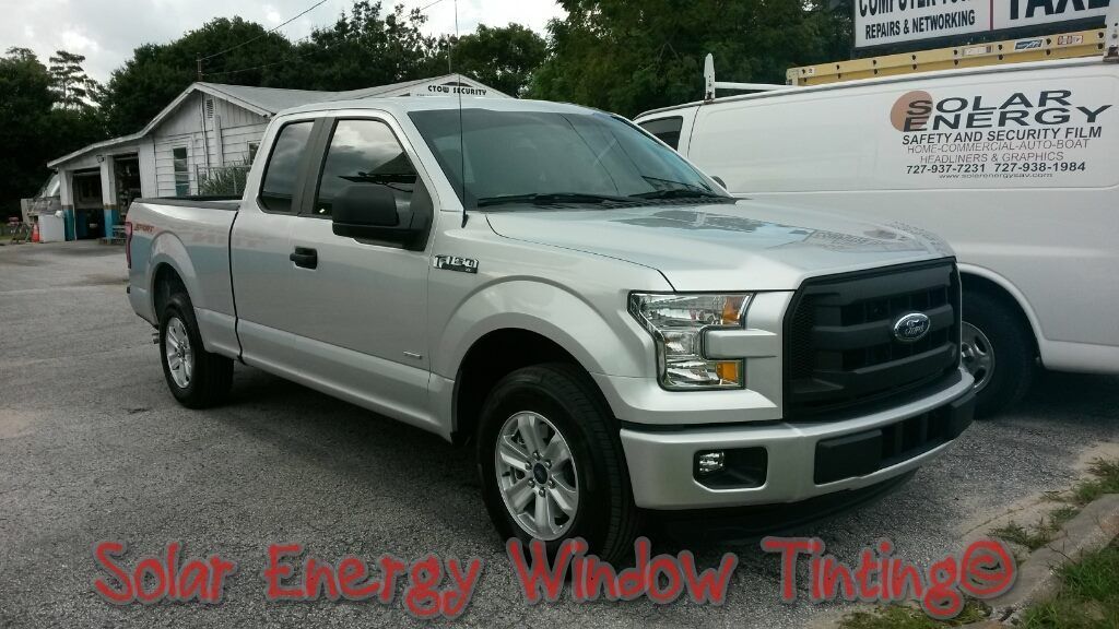 A silver Ford F-150 pickup truck parked on a gravel lot next to a white van with Solar Energy Window Tinting branding.