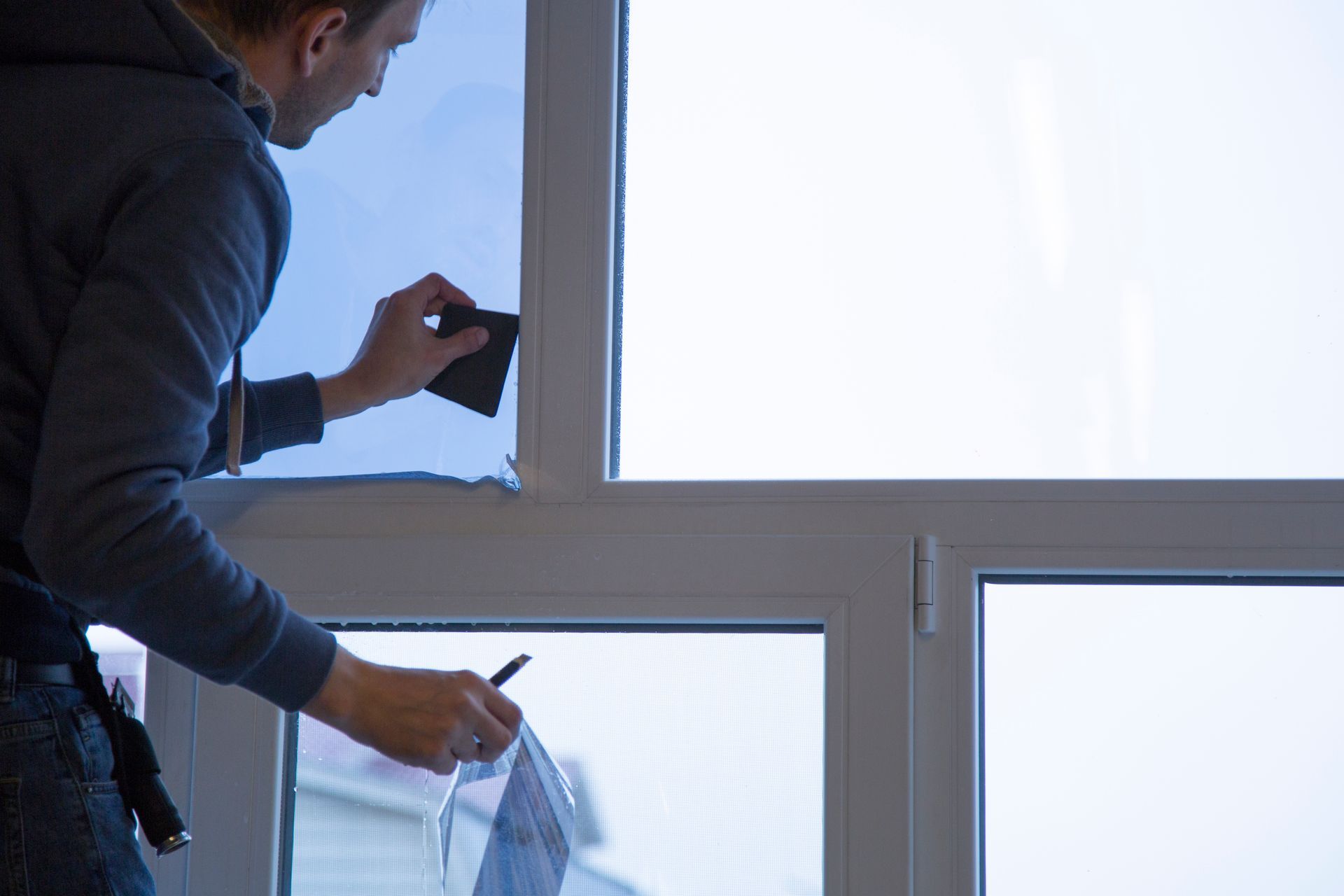 A person applies window tint film to a pane using a squeegee tool.