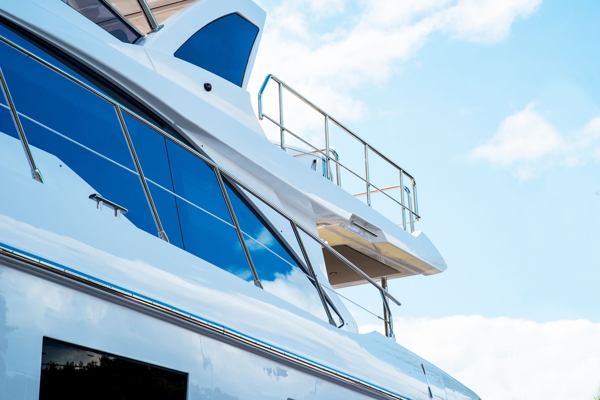 The side and deck area of a modern white yacht against a bright blue sky with light clouds.