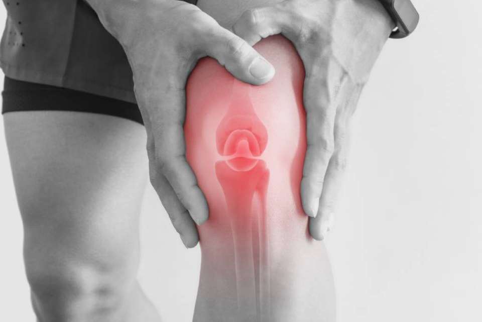 Persona che tiene il ginocchio, evidenziando il dolore. La luce rossa mette in risalto l'articolazione del ginocchio.