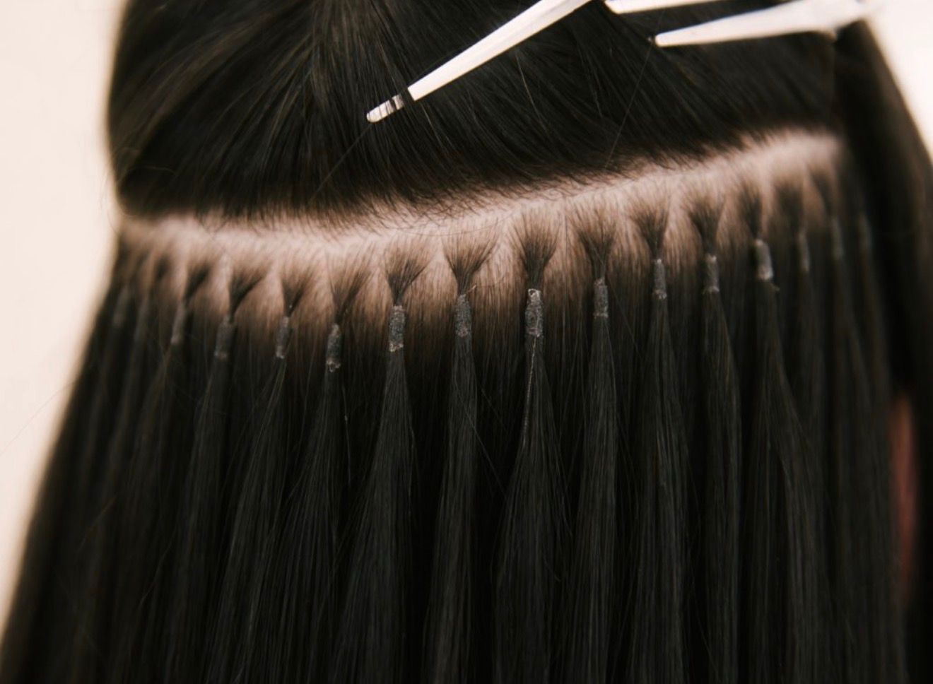 Close-up view of black hair extensions attached to natural hair at the scalp using small, individual keratin bonds.