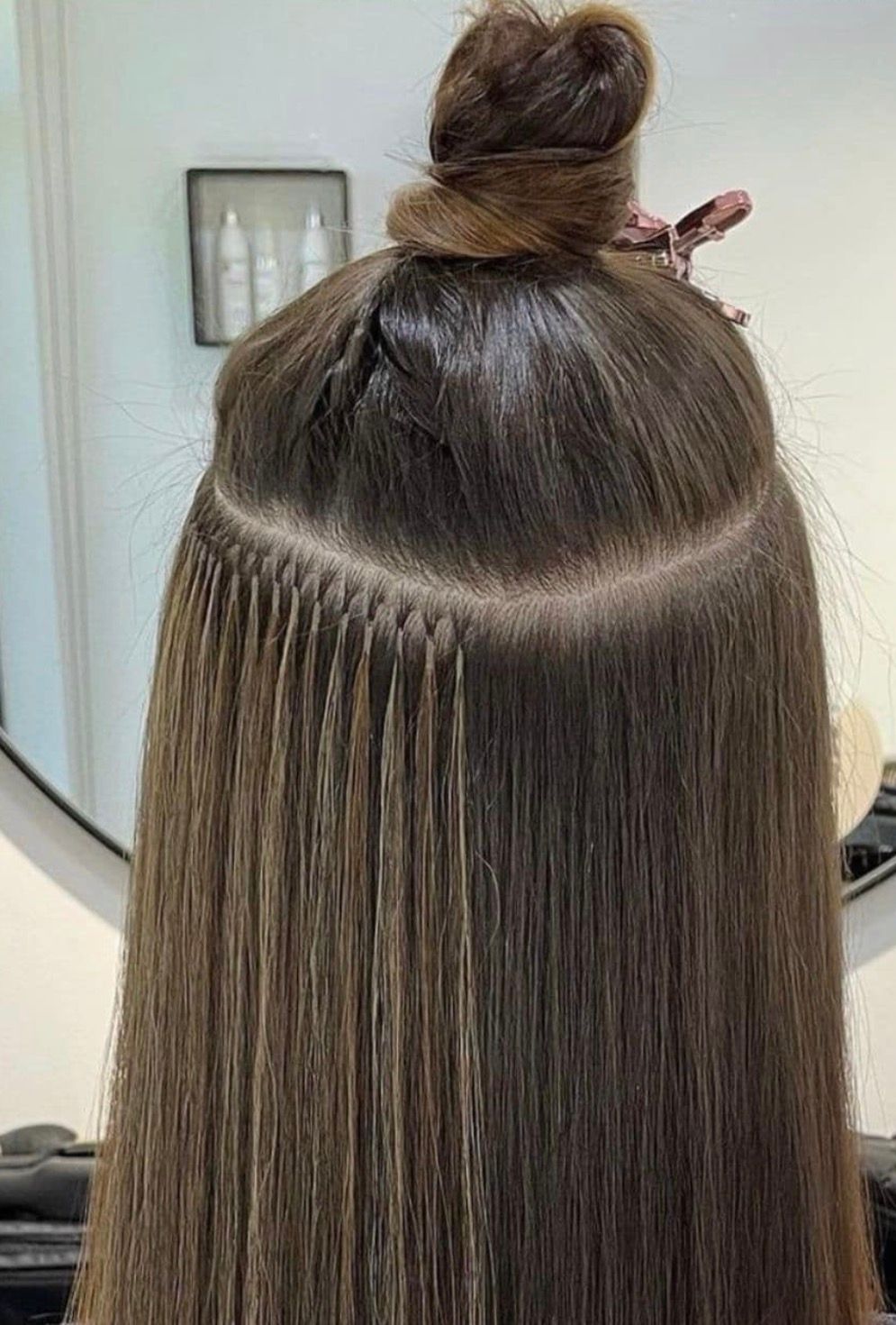 A close-up of brown hair featuring a row of installed micro-link or bead hair extensions in a salon setting.