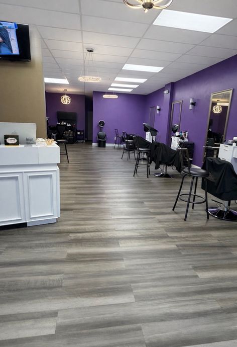 The interior of a hair salon with grey wood floors, white reception desk, and purple walls with styling stations.