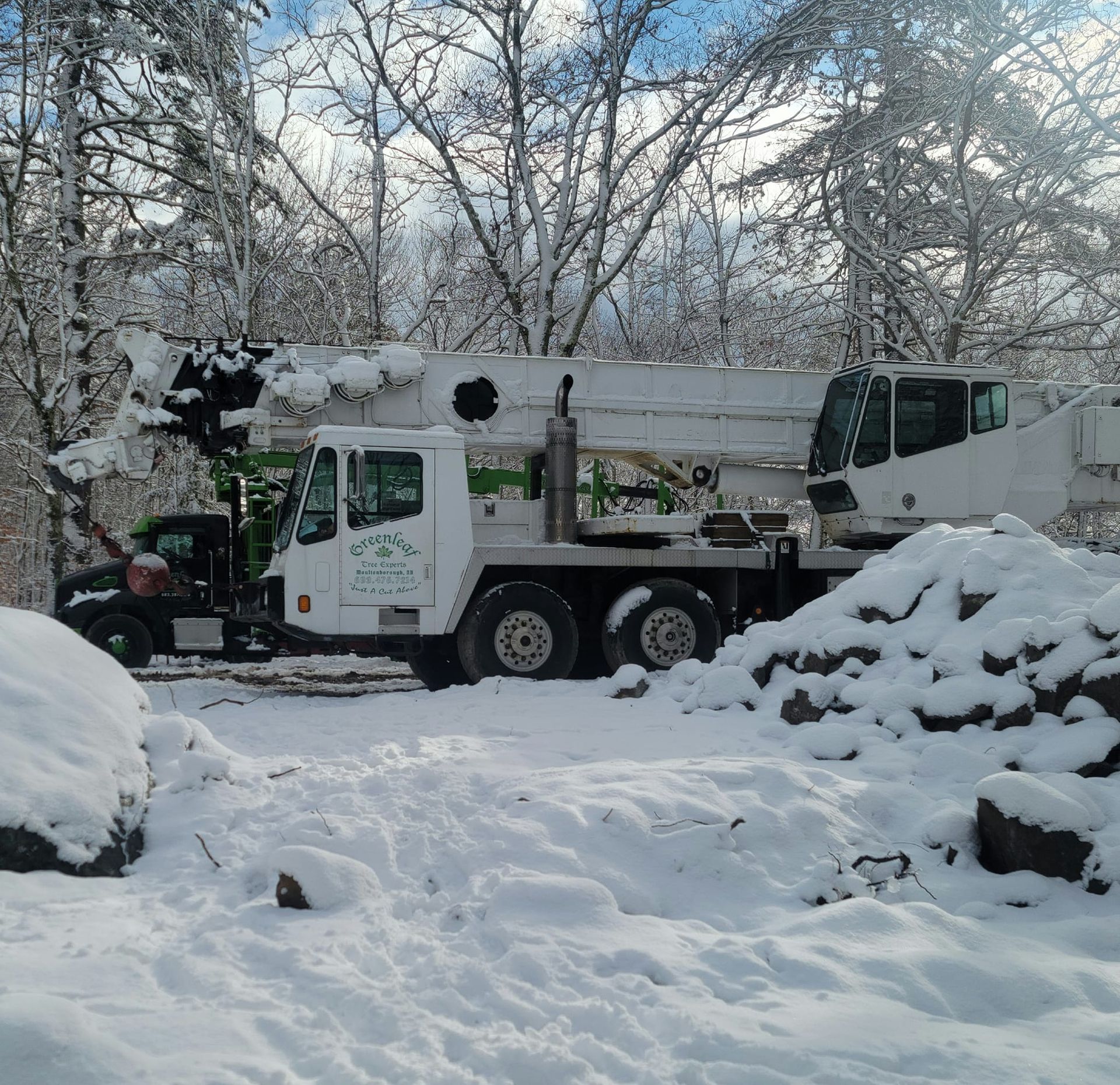 A white truck with a crane on the back is parked in the snow