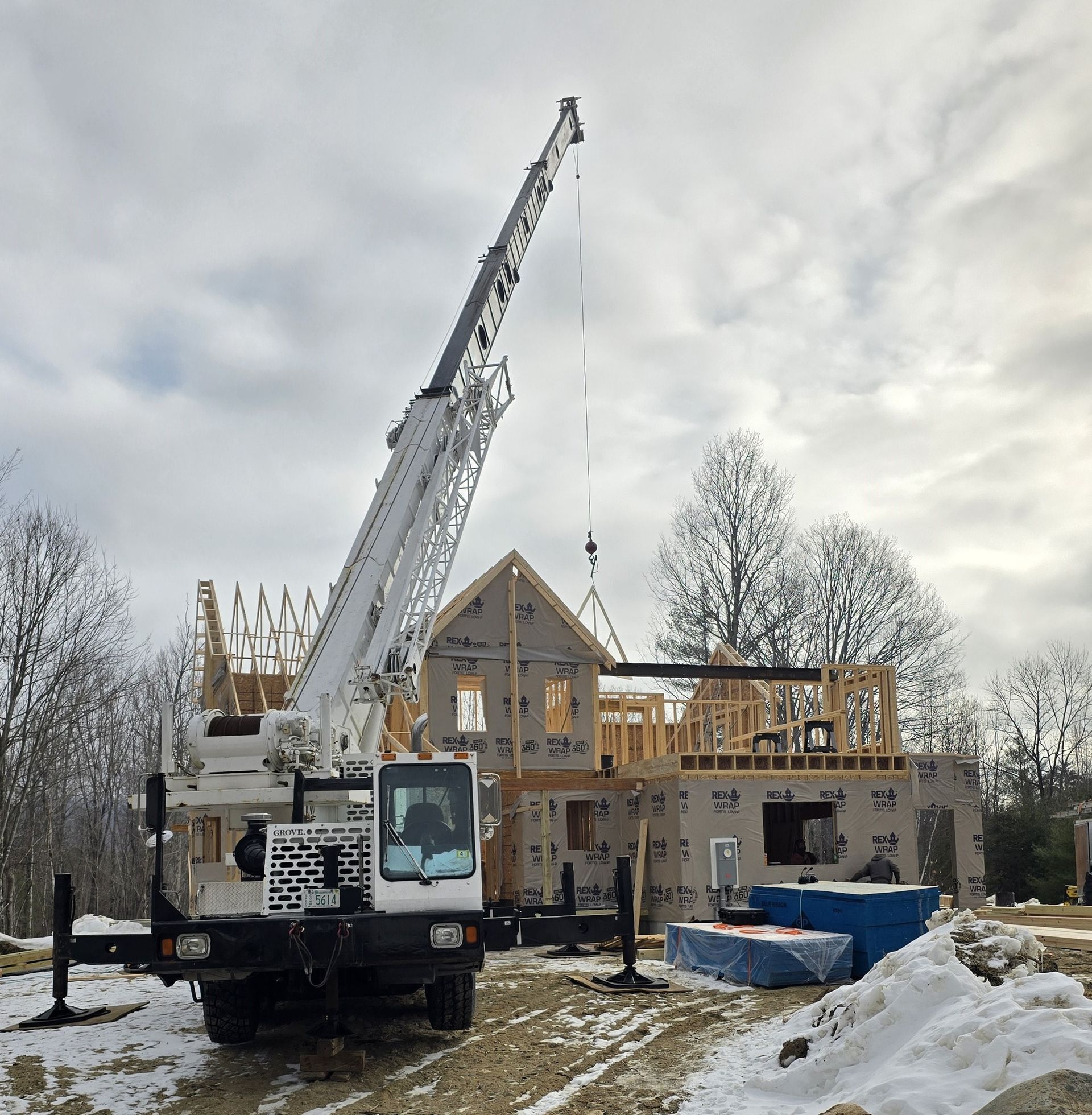 A large white crane is parked in front of a house under construction