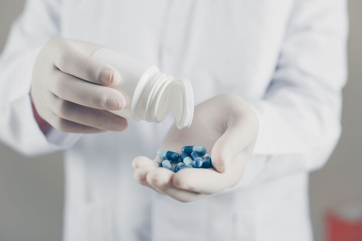 a doctor is pouring pills from a bottle into his hand .