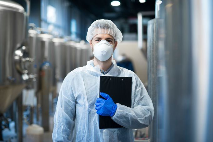 a man wearing a mask and gloves is holding a clipboard in a factory .