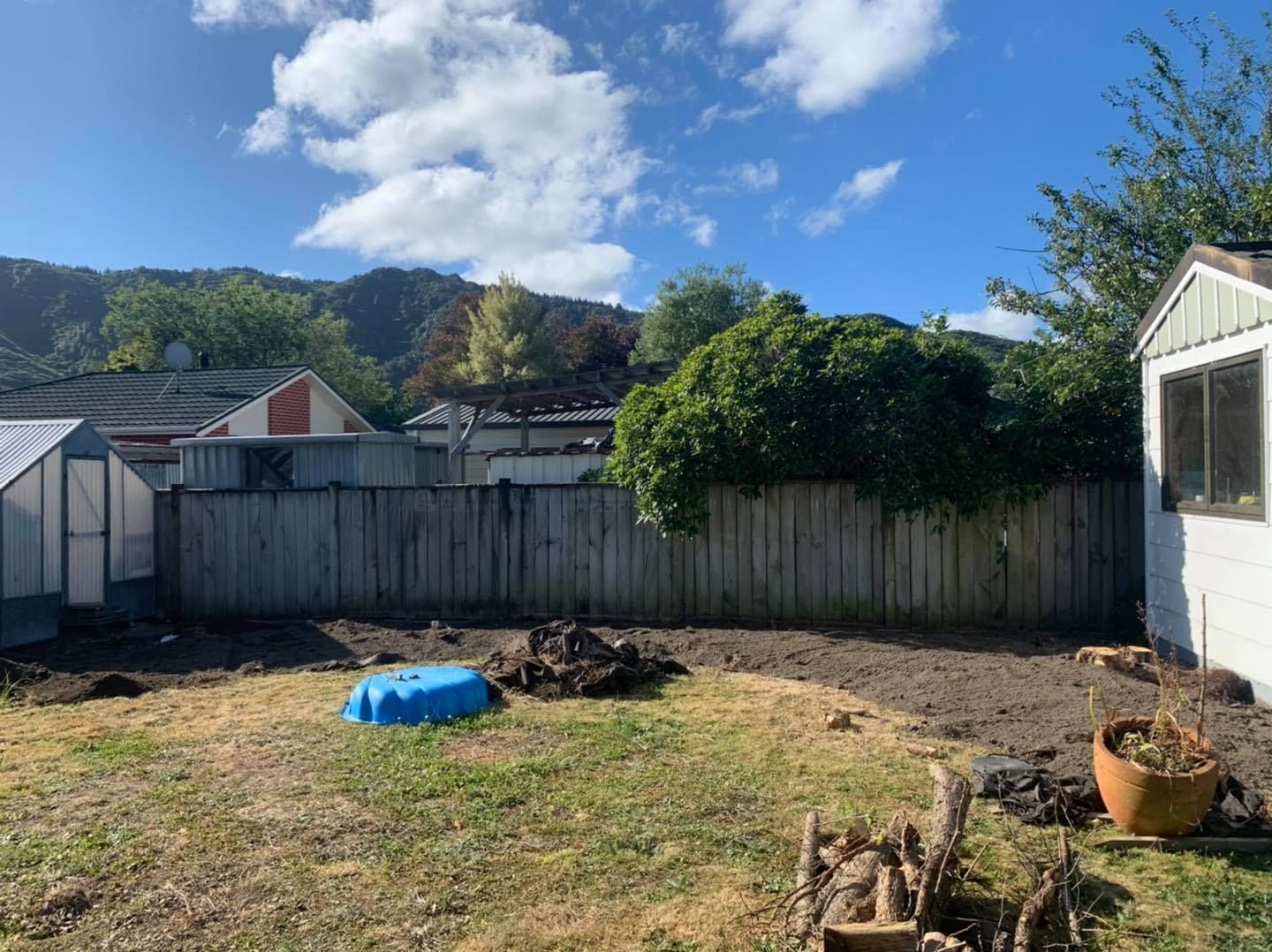 A backyard with a wooden fence and a greenhouse in the background.