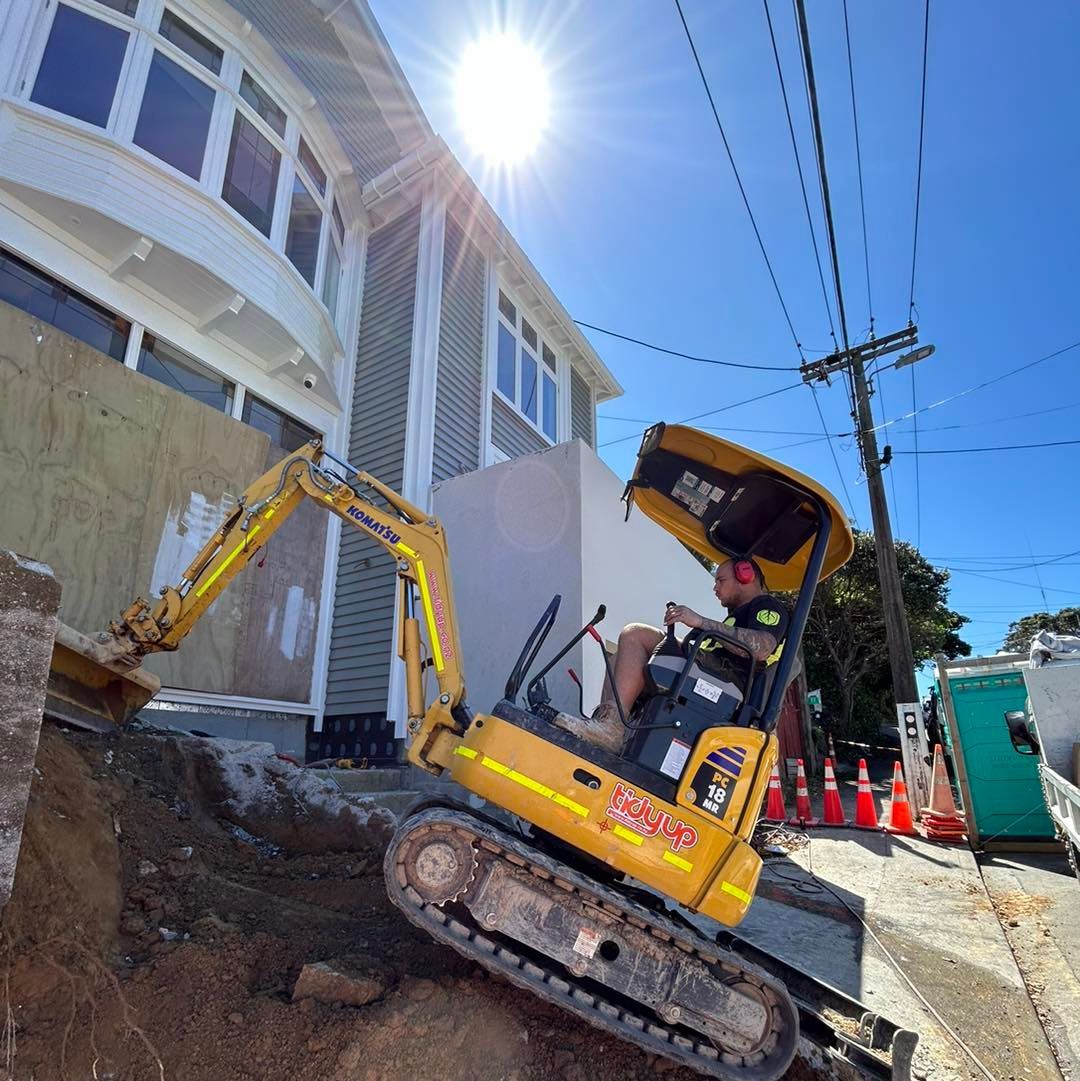 A man is driving a yellow excavator in front of a building.
