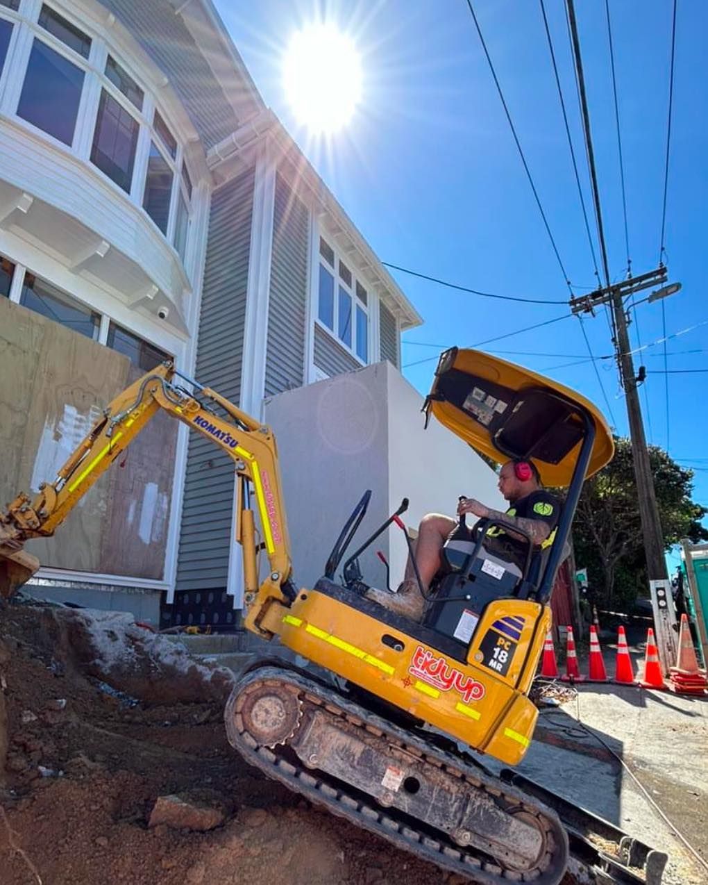 A man is driving a yellow excavator next to a building.