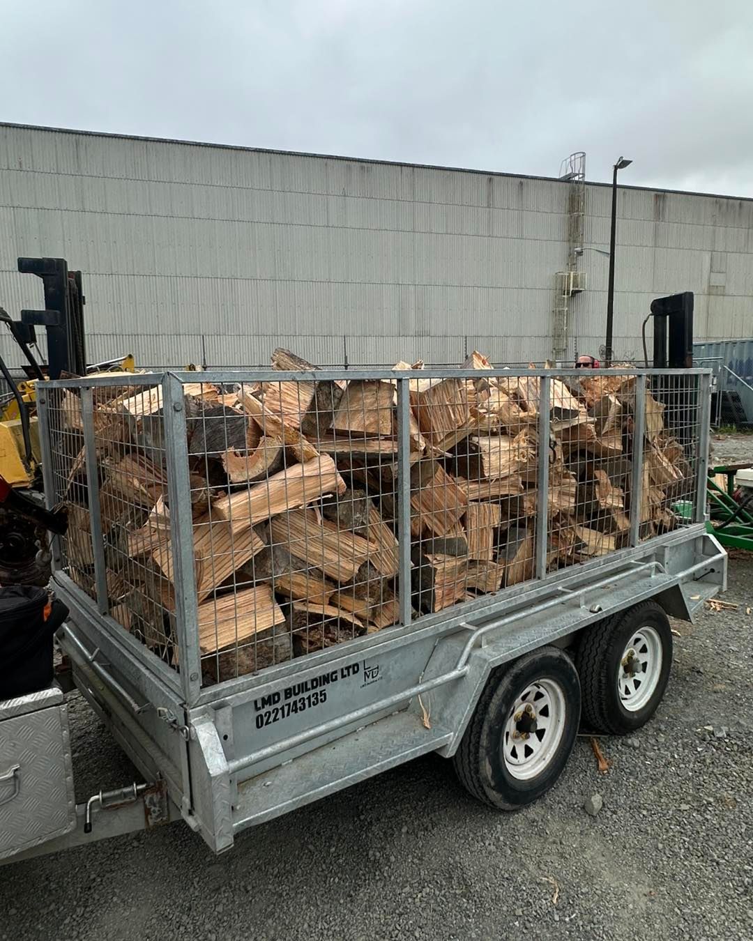 A trailer filled with logs is parked in front of a building.