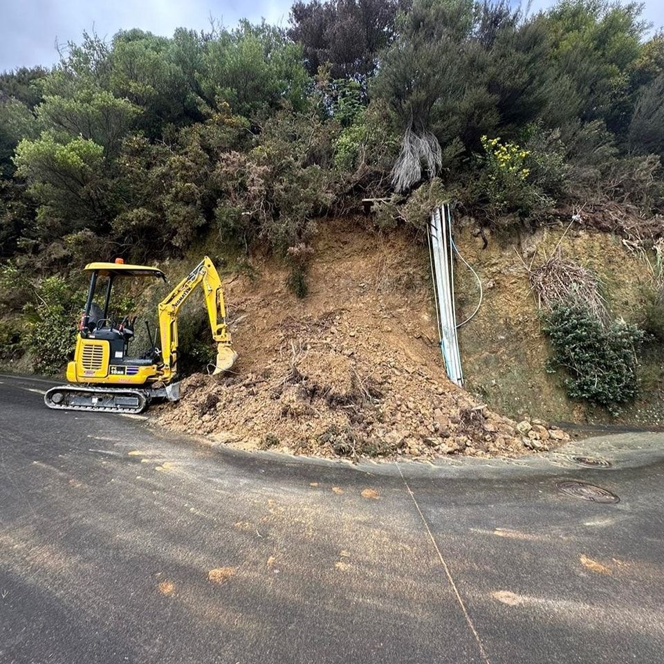 A yellow excavator is working on a hillside next to a road.