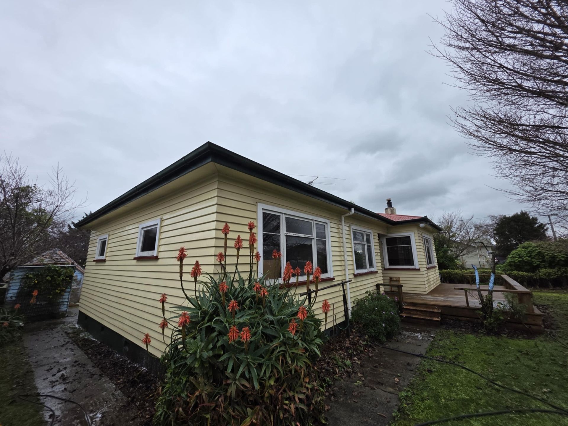 A small yellow house with flowers in front of it on a cloudy day.