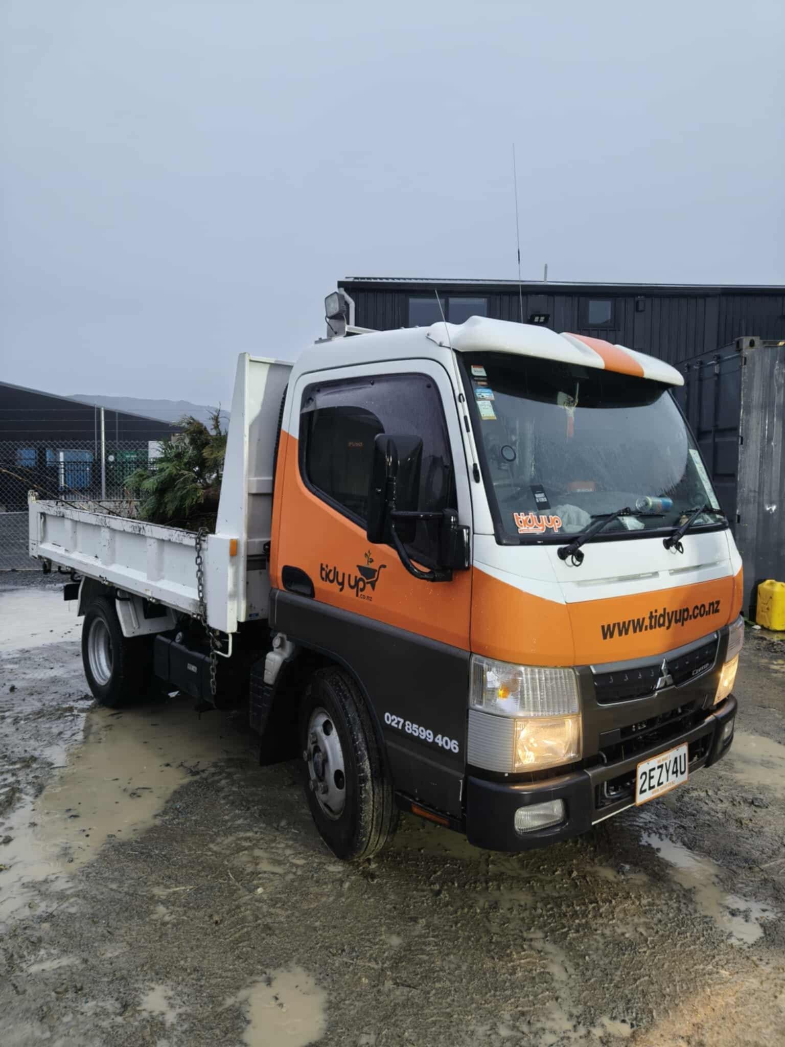 An orange and white dump truck is parked in a muddy lot.