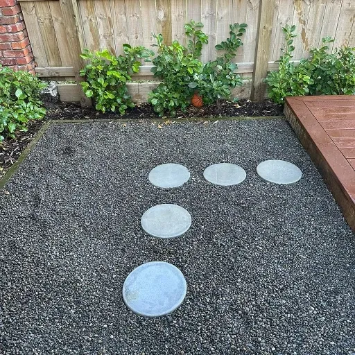 A patio with a wooden fence and concrete stepping stones.
