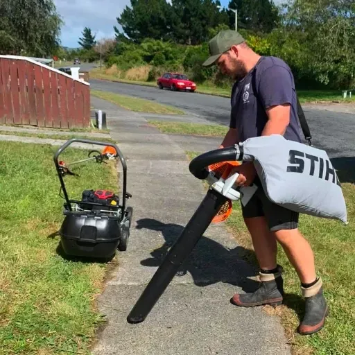 A man is using a stihl blower on the sidewalk