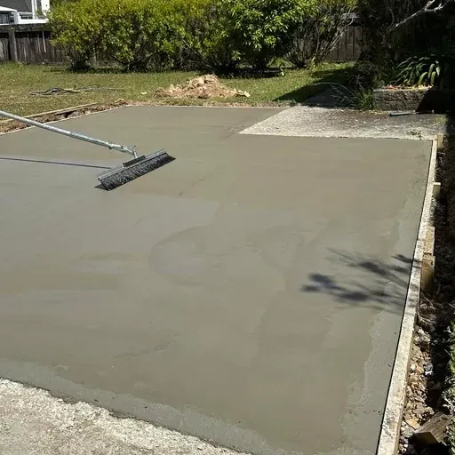 A broom is being used to smooth a concrete driveway.