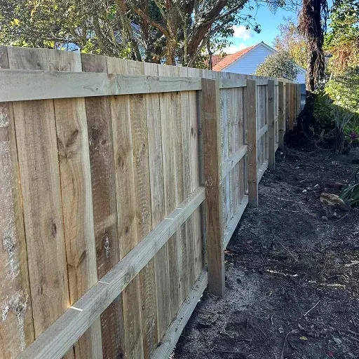 A wooden fence is sitting on top of a dirt path next to a house.