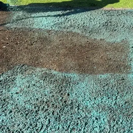 A person is spreading green fertilizer on a dirt field.