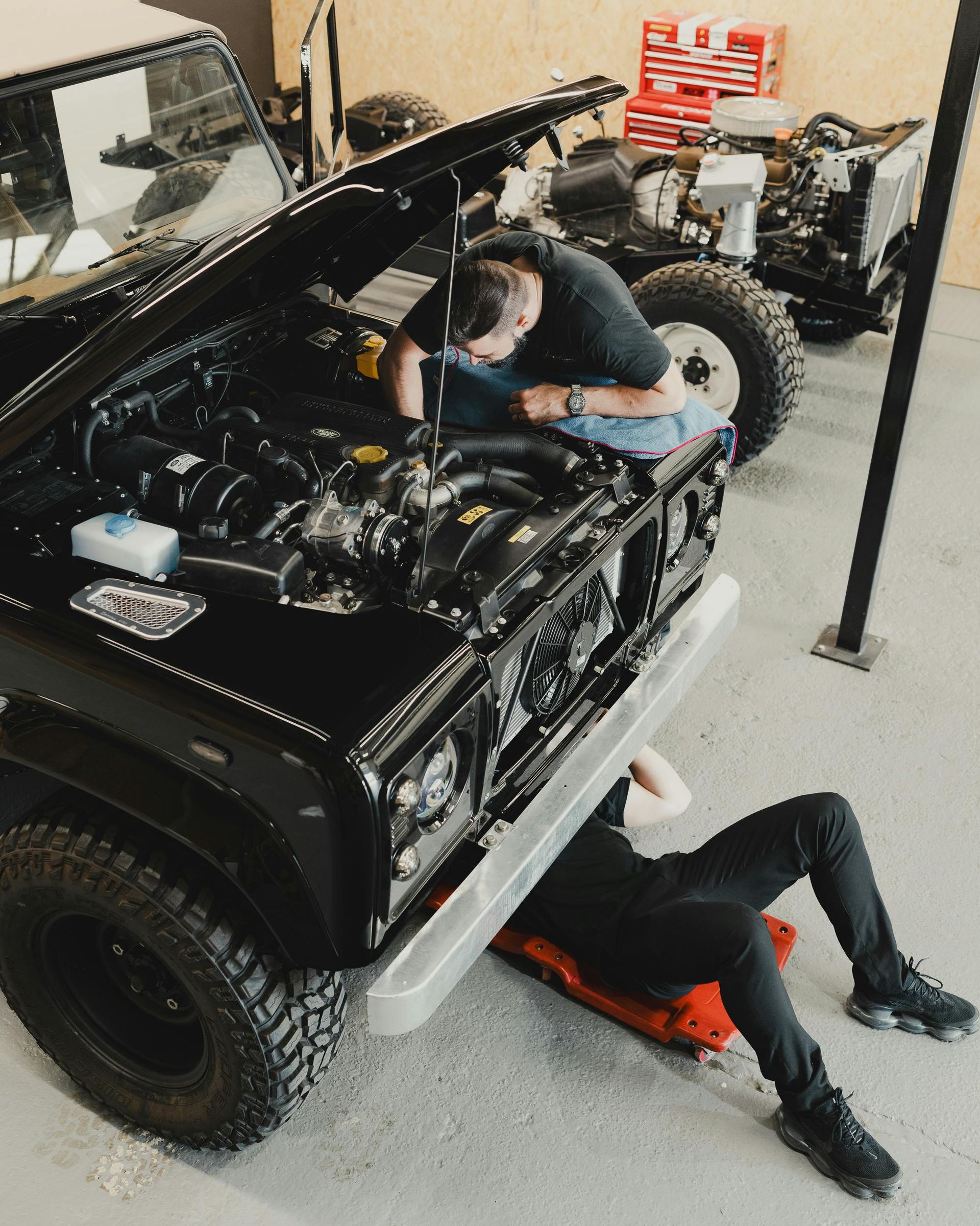Two men are working on a black jeep in a garage.
