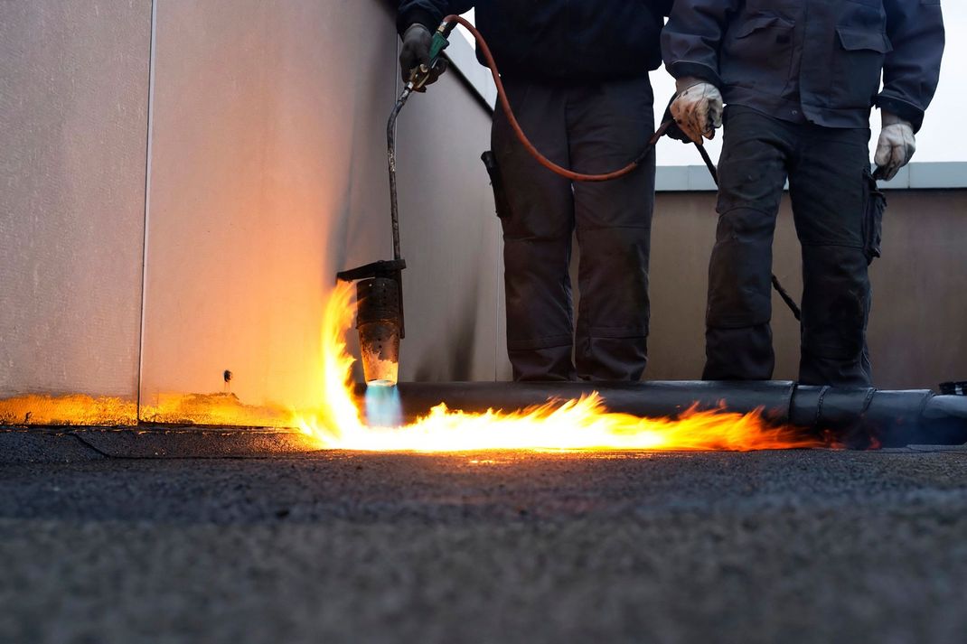Durante l'installazione, gli operai, muniti di dispositivi di protezione, utilizzano una torcia a propano per fondere la membrana di copertura contro una parete.