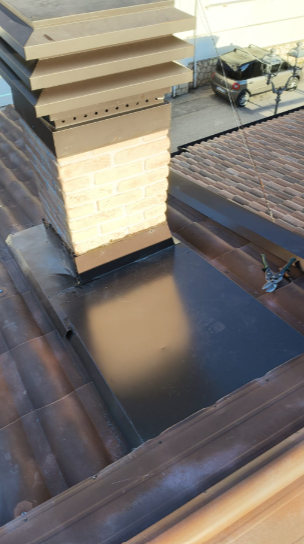 Un camino beige con comignolo a più livelli, caratterizzato da una lamiera nera su un tetto di tegole marroni, visto dall'alto.