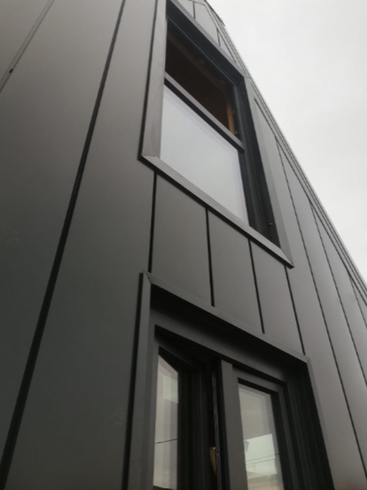 Vista dal basso dell'esterno di un edificio moderno caratterizzato da rivestimenti in pannelli verticali neri opachi e infissi rettangolari.