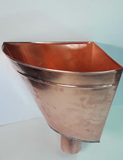 Un pluviale o collettore di grondaia in rame lucido, montato ad angolo, con un tubo di scarico rivolto verso il basso.