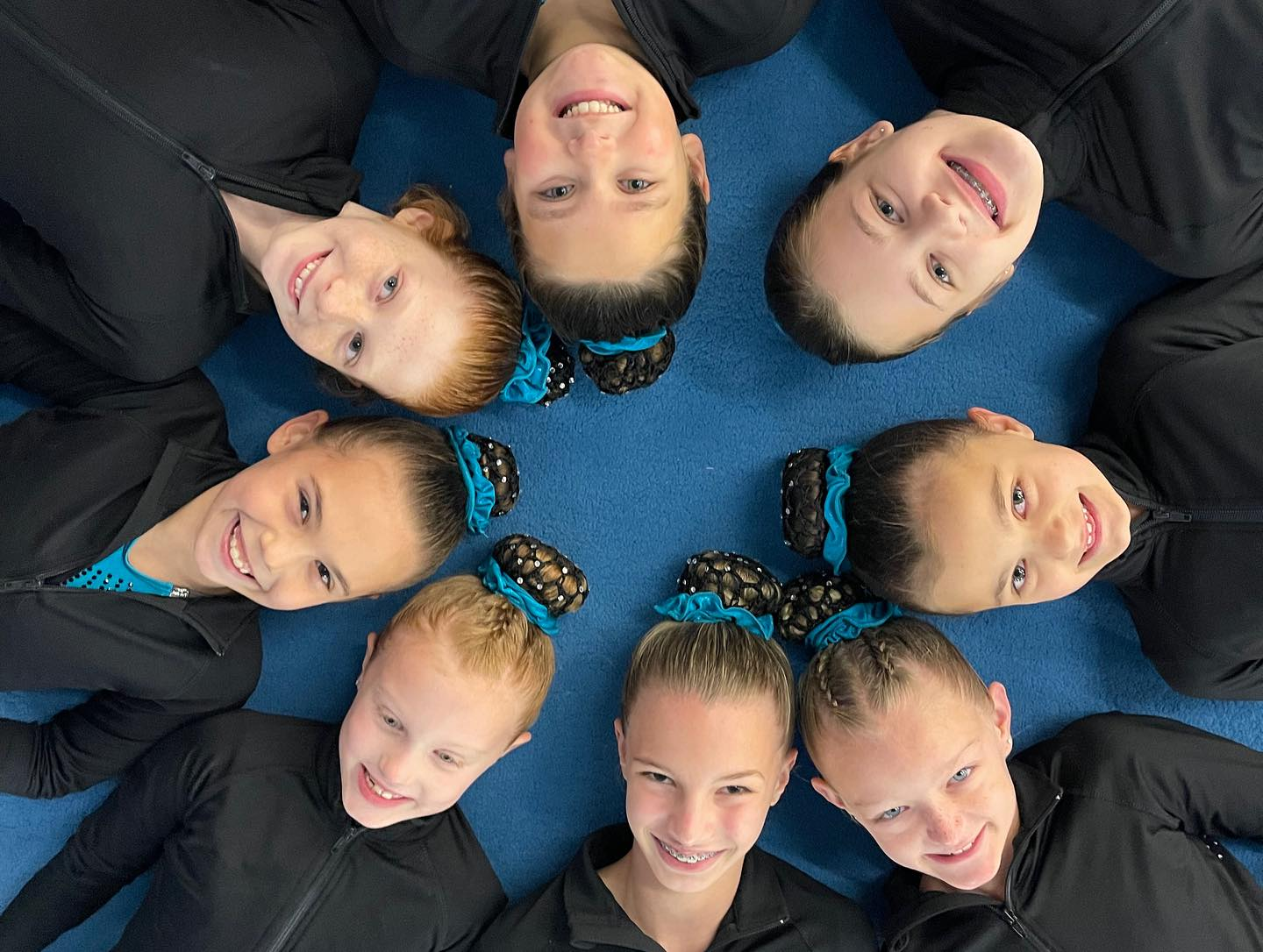 A group of young girls are laying in a circle on the floor.