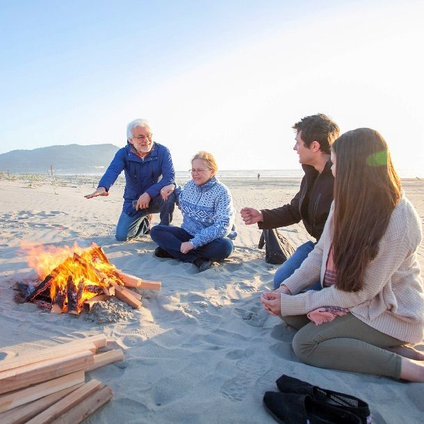 a group of people are sitting around a fire on the beach
