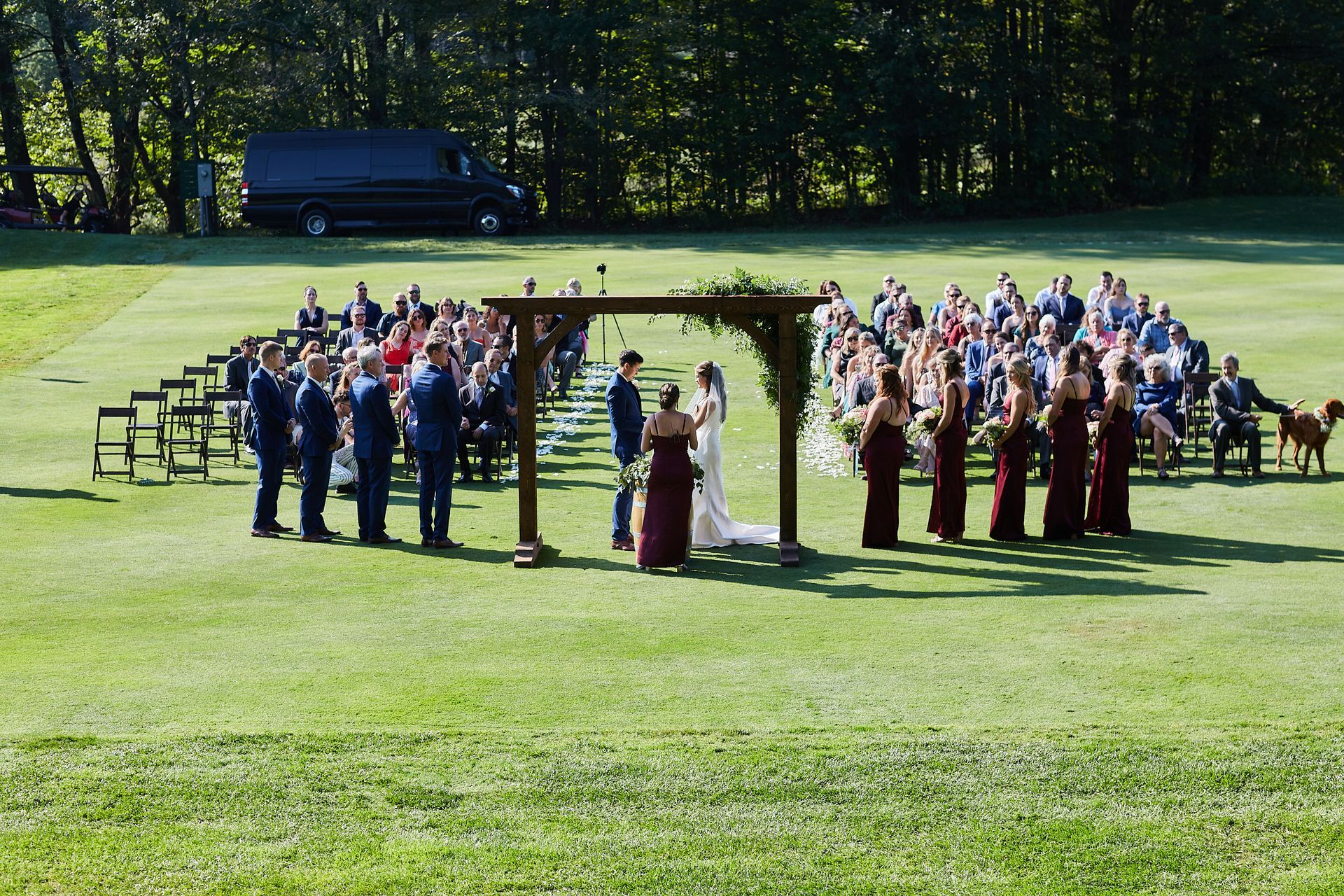 A large group of people are standing in a field during a wedding ceremony.