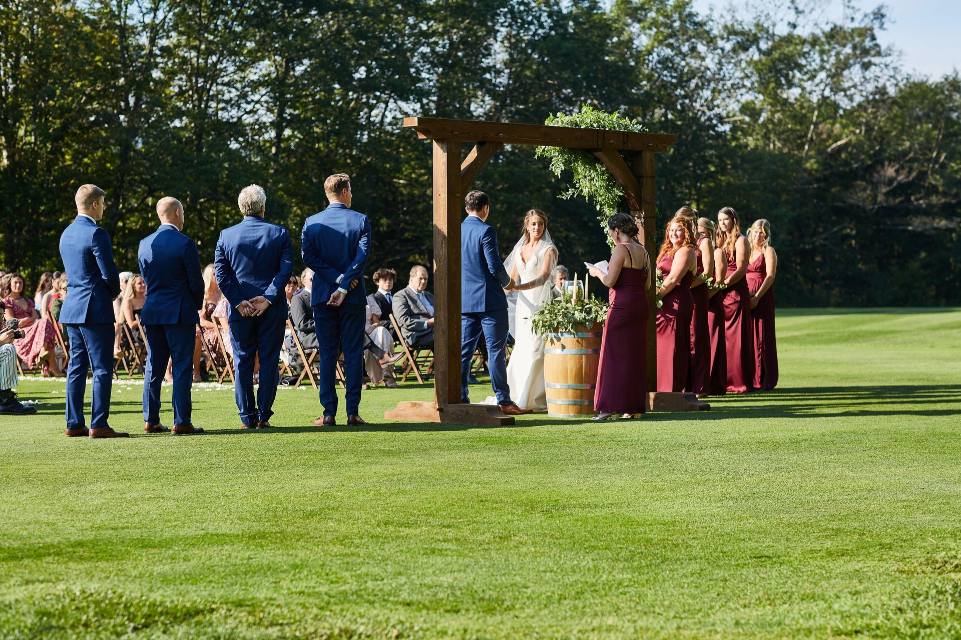A bride and groom are getting married in a field with their wedding party.