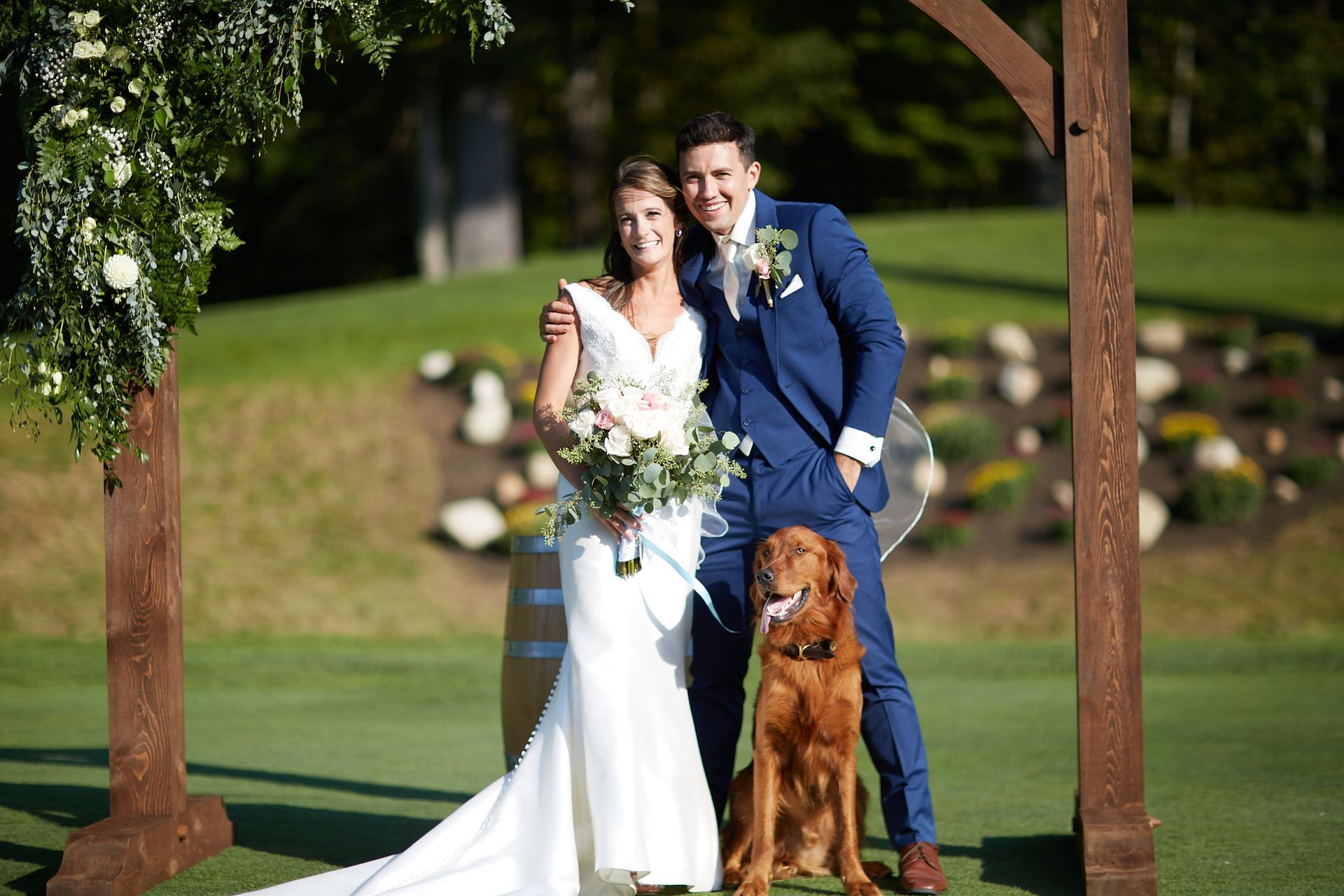 A bride and groom are posing for a picture with their dog.