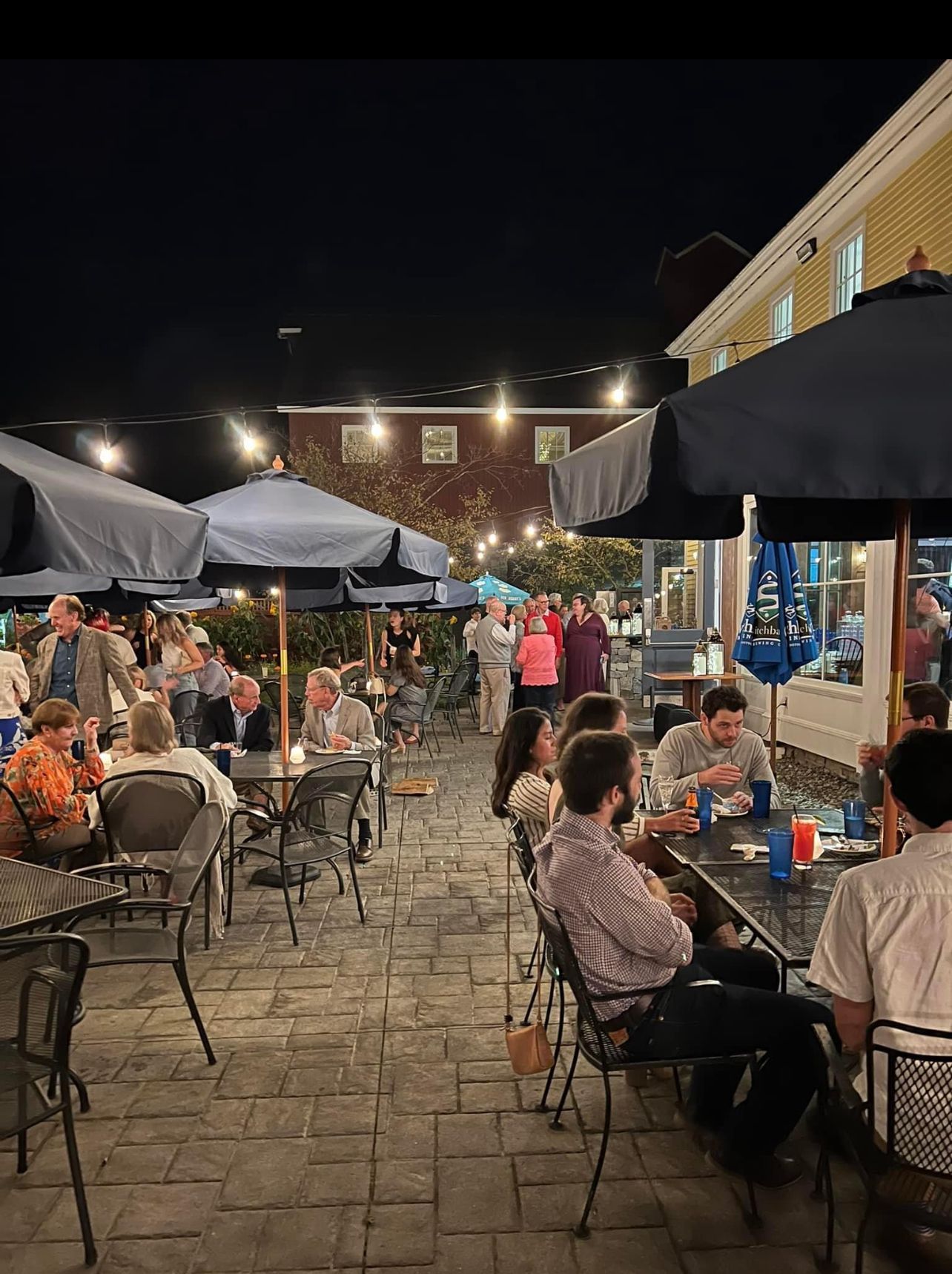 Outdoor patio at night; people seated at tables under umbrellas, socializing.