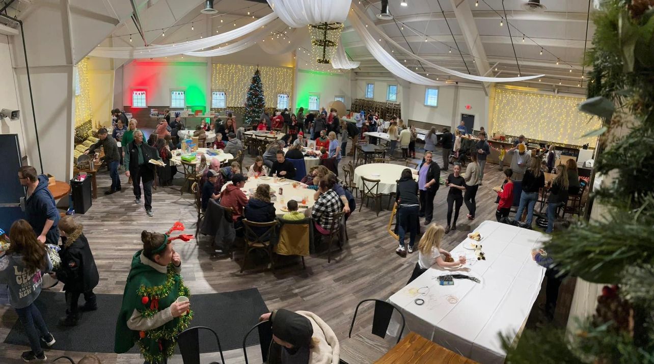 Holiday party with many people in a large room, decorated with lights and a Christmas tree.