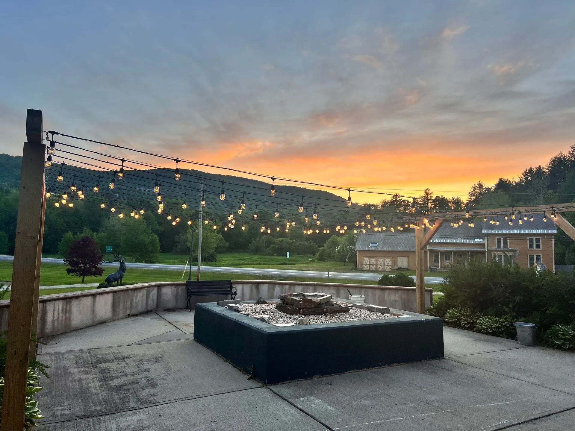 Sunset over a patio with string lights, fire pit, and buildings.