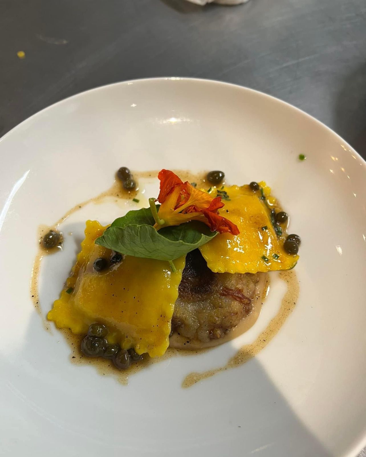 Yellow ravioli with capers, basil, and flower garnish on a white plate.