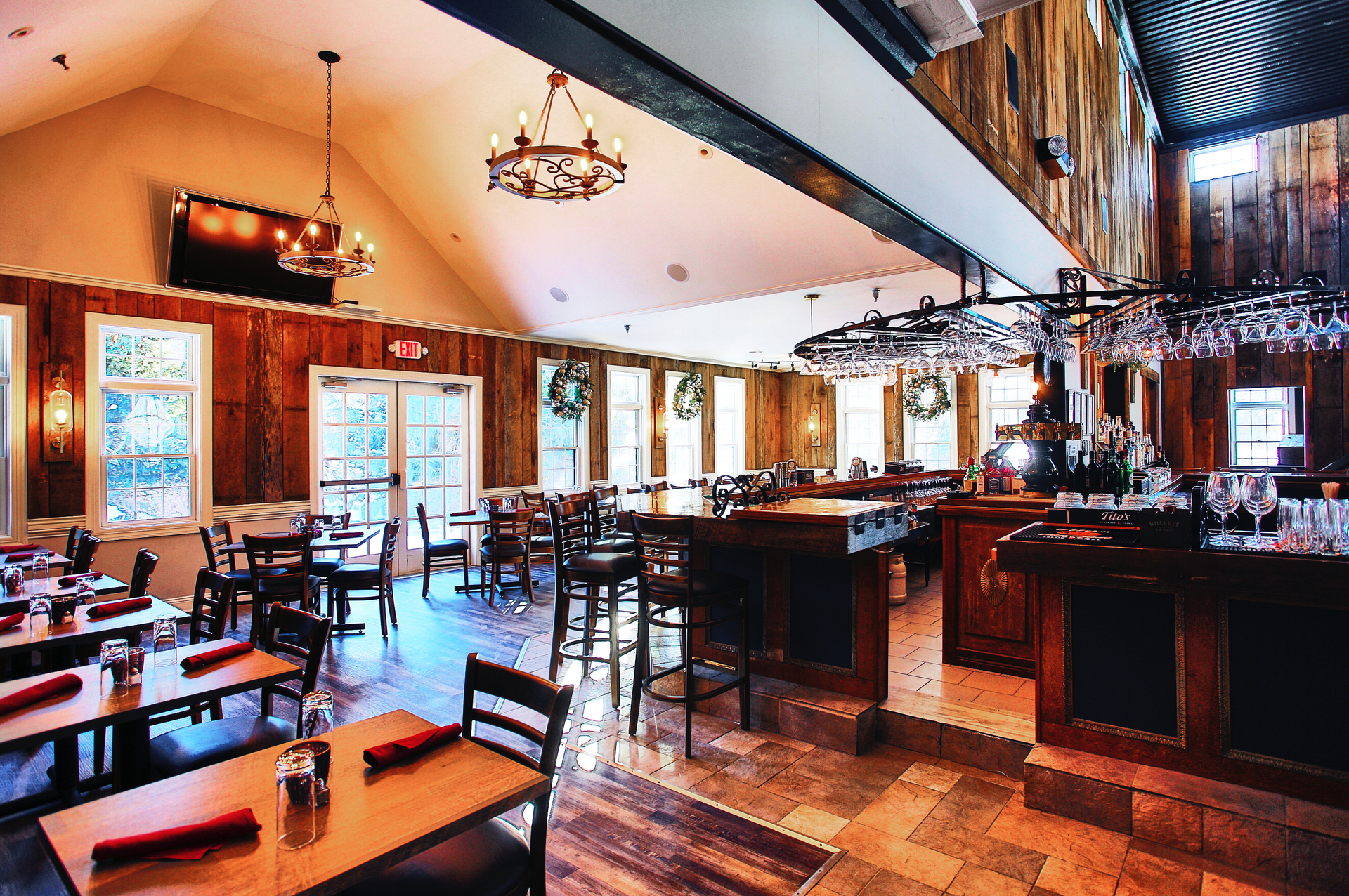 Restaurant interior with wooden walls, tables, bar, and chandeliers.
