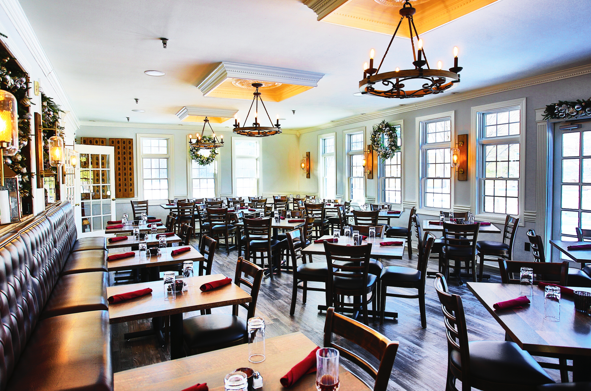 Restaurant interior: tables, chairs, chandeliers, windows, and booths; warm tones.