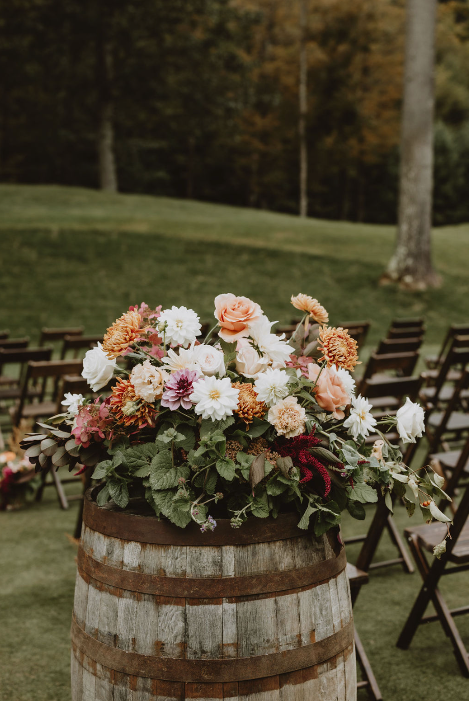 A wooden barrel filled with flowers is sitting on top of a lush green field.