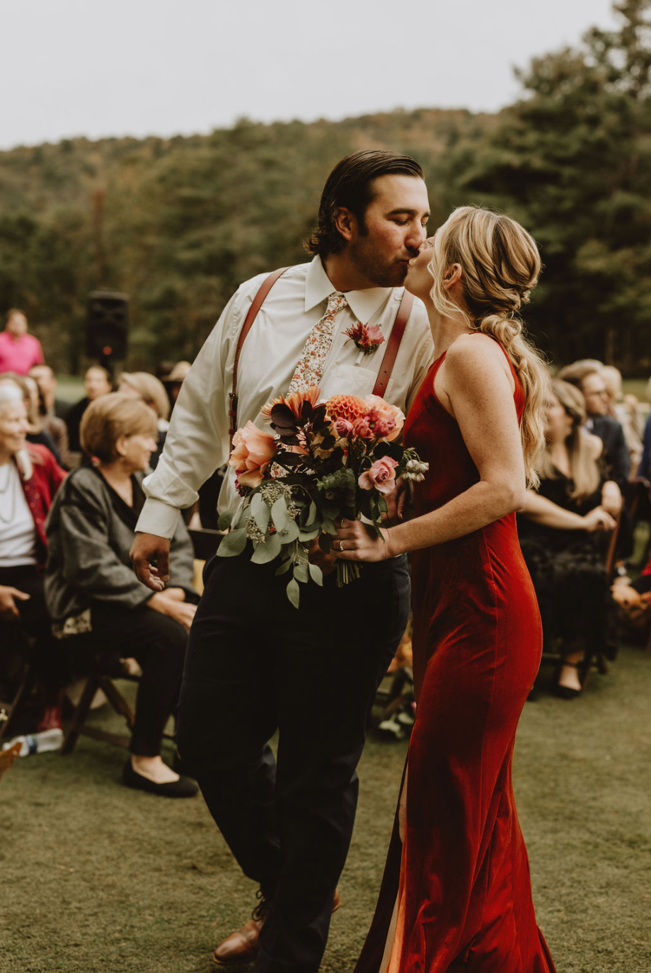 A bride and groom are kissing while walking down the aisle at their wedding.