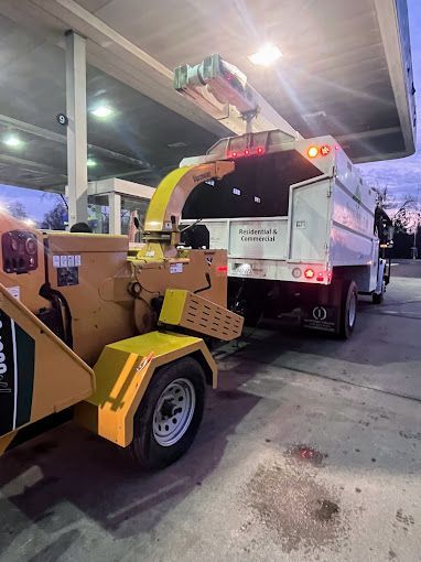 A tree chipper is parked next to a truck at a gas station.