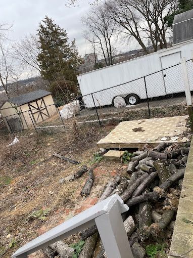 A white trailer is parked in a yard next to a pile of logs.