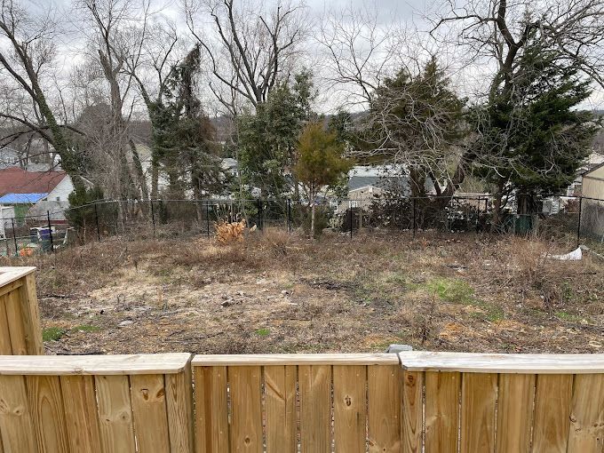A wooden fence surrounds a dirt field with trees in the background.